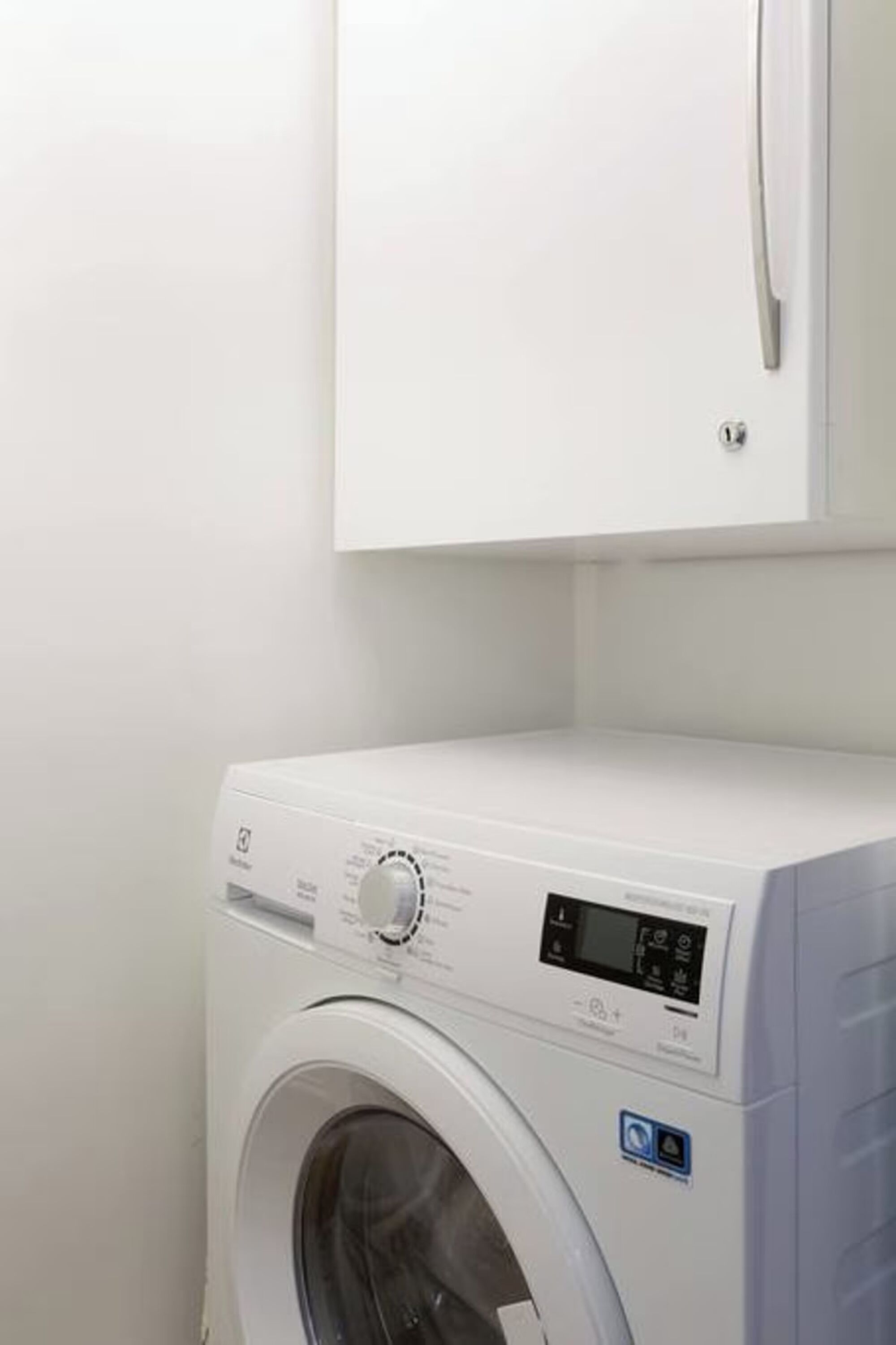 Une machine à laver à chargement frontal, dans une pièce aux murs blancs.