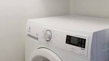 A front-loading washing machine in a white-walled room.