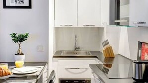 A compact kitchen with white cabinets, a stainless steel sink, and a dishwasher. - Le Marais Gem (Paris)