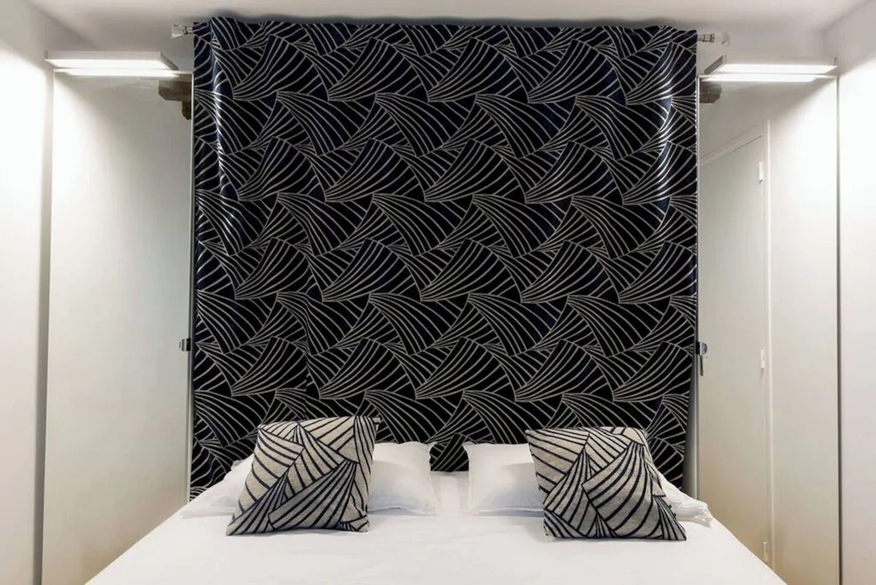 A hotel room with a bed, two pillows, and a patterned curtain.