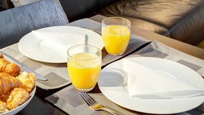 A breakfast setup with croissants and orange juice on a table, a sofa with cushions, a mirror, and a lamp in a room. - Le Marais Gem (Paris)