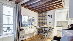 A compact living space with a dining area, kitchenette, and a large window with curtains. - Le Marais Gem (Paris)