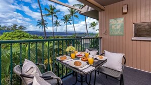 A balcony with a table set for breakfast, overlooking a scenic view with palm trees and the ocean.