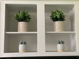 A white cabinet with two shelves, each holding a potted plant.