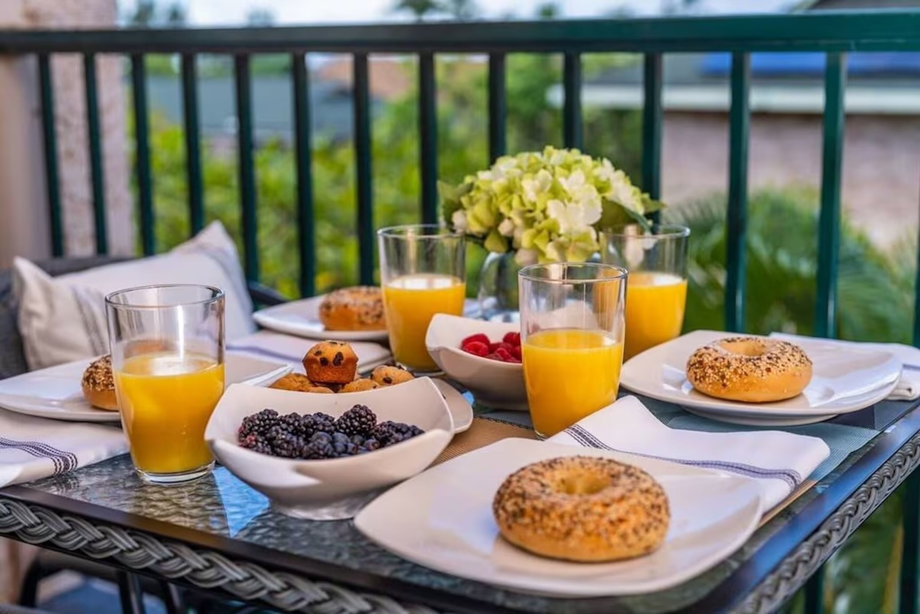 Ein Frühstückstisch auf einem Balkon mit Speisen, Orangensaftgläsern und einem Blumenstrauß.