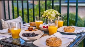 Ein Frühstückstisch auf einem Balkon mit Speisen, Orangensaftgläsern und einem Blumenstrauß.