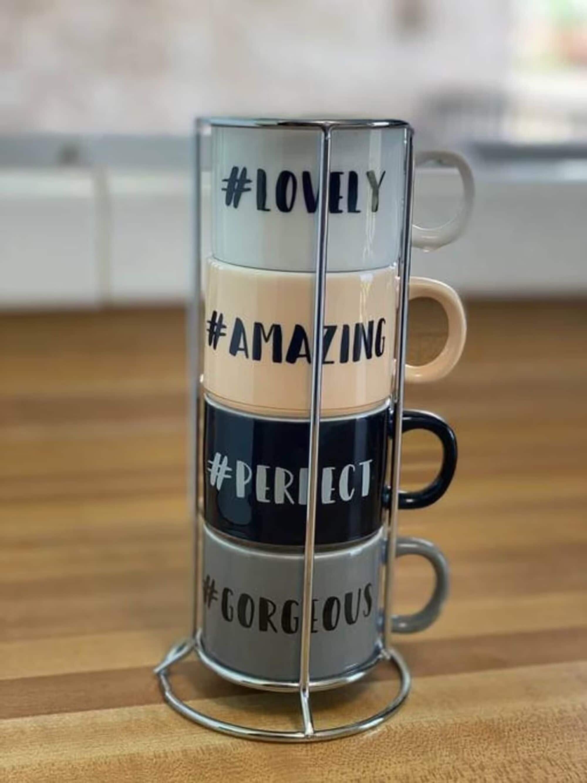 Ein Glas-Untertassenhalter mit vier Tassen, jede beschriftet mit einem Hashtag und einem positiven Adjektiv.