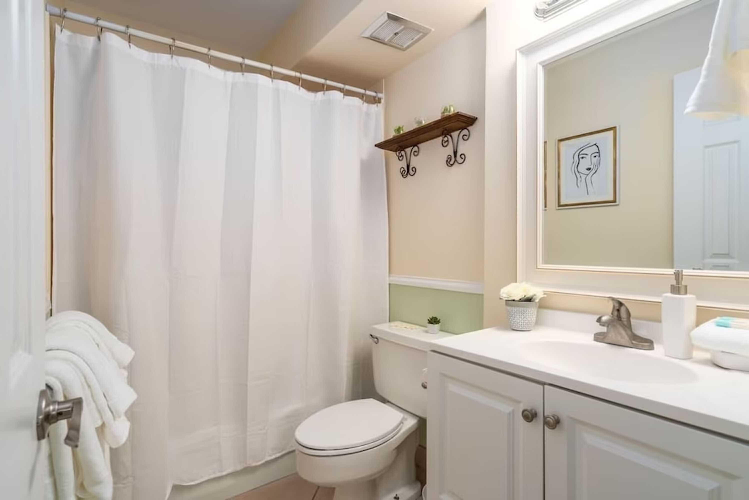 Une salle de bain équipée d’une douche avec rideau, de toilettes, d’un lavabo et d’un miroir orné d’un tableau encadré.