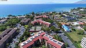 An aerial view of a coastal resort with multiple buildings, parking areas, and a view of the ocean.