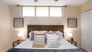A bedroom with a large bed, two bedside tables with lamps, a wooden headboard, and two framed artworks on the walls.