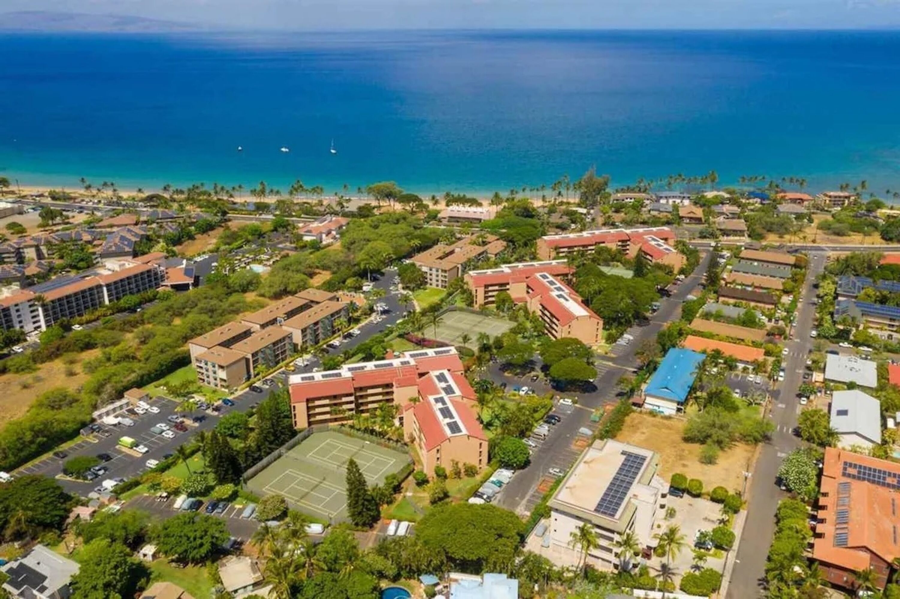 Vue aérienne d’un quartier résidentiel situé sur la côte, avec de nombreux immeubles, des routes et un court de tennis.
