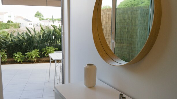 Un baño con tocador blanco, espejo redondo y vistas a un jardín a través de una puerta corrediza.