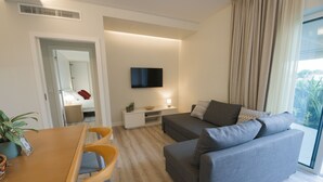 Una sala de estar moderna con un sofá gris, una mesa de comedor de madera y un televisor de pantalla plana montado en la pared.