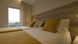 Habitación de hotel con dos camas, cabecero de madera, ventana con cortinas y mesita de noche.