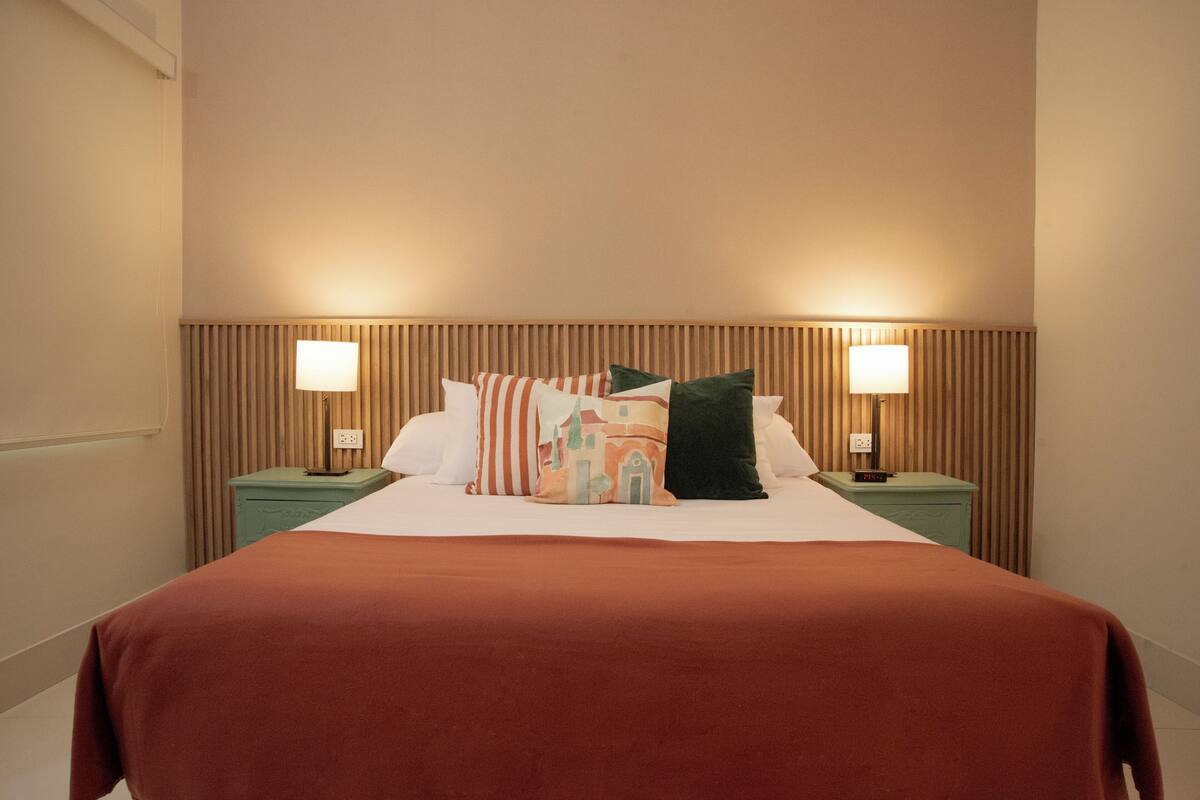 A neatly made bed with a brown bedspread, two bedside tables with lamps, and a wooden headboard.