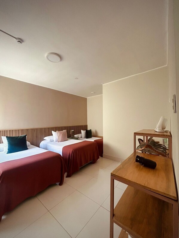 A hotel room with two beds, a wooden desk, a fan, and a shoe rack. - Lima Atelier (Lima)