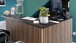 A reception desk with a computer, a potted plant, and a QR code sign. - Lima Atelier (Lima)
