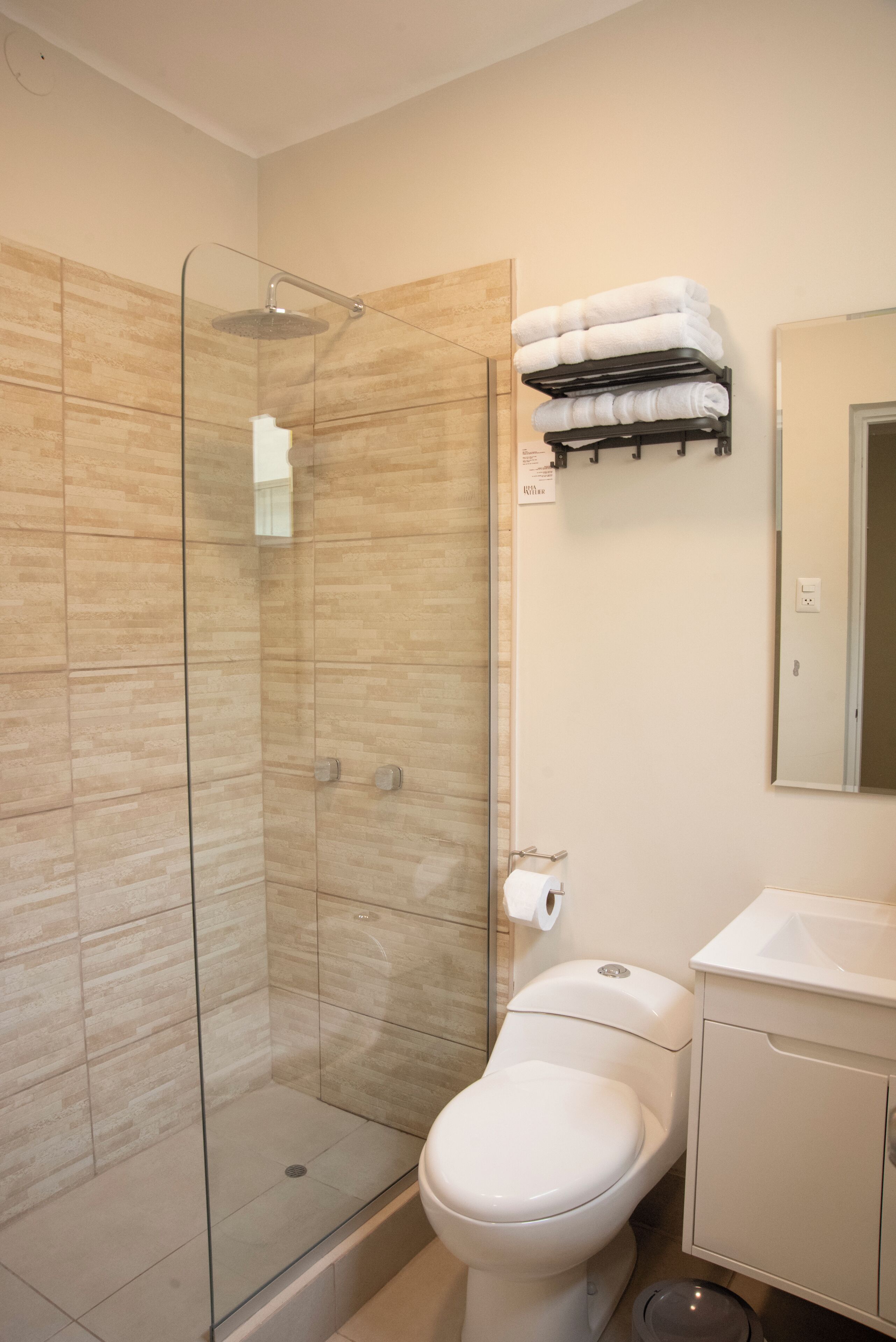 Een badkamer met een douchecabine van glas, een toilet, een wastafel en een handdoekrek met opgevouwen handdoeken.