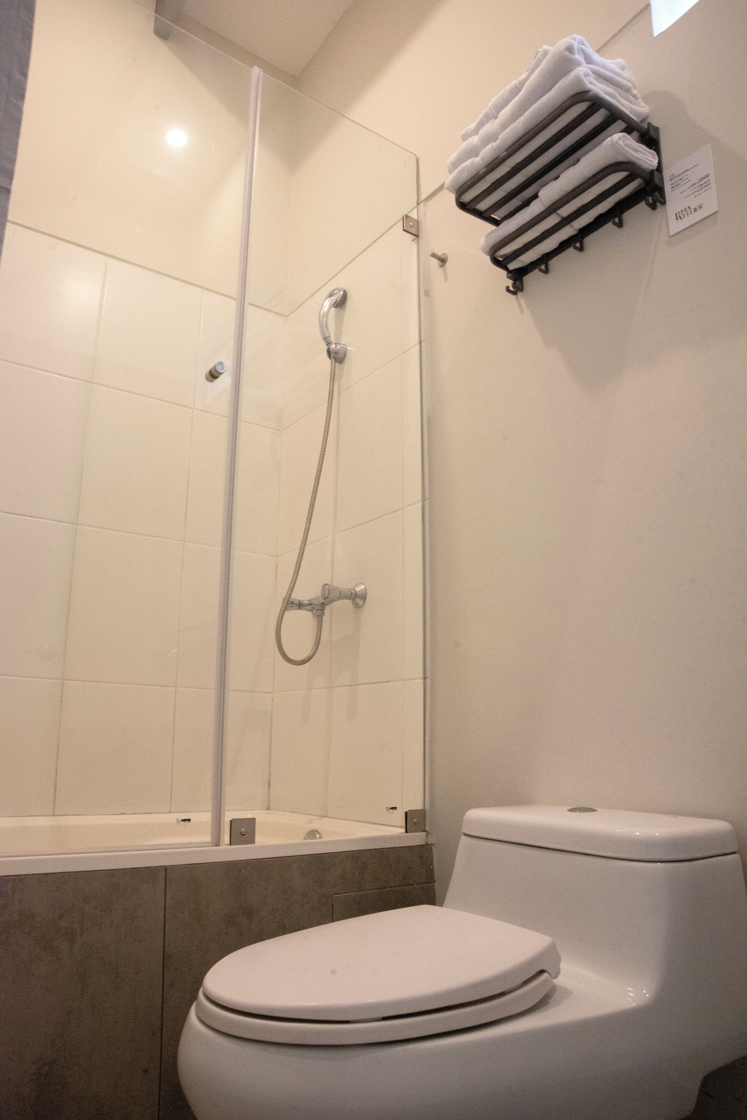 A bathroom with a glass-enclosed shower, a white toilet, and a towel rack with folded towels.