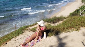 Eine Strandansicht mit einer Person, die auf einem Handtuch entspannt, einem Strandsonnenschirm und einer Wasserflasche.