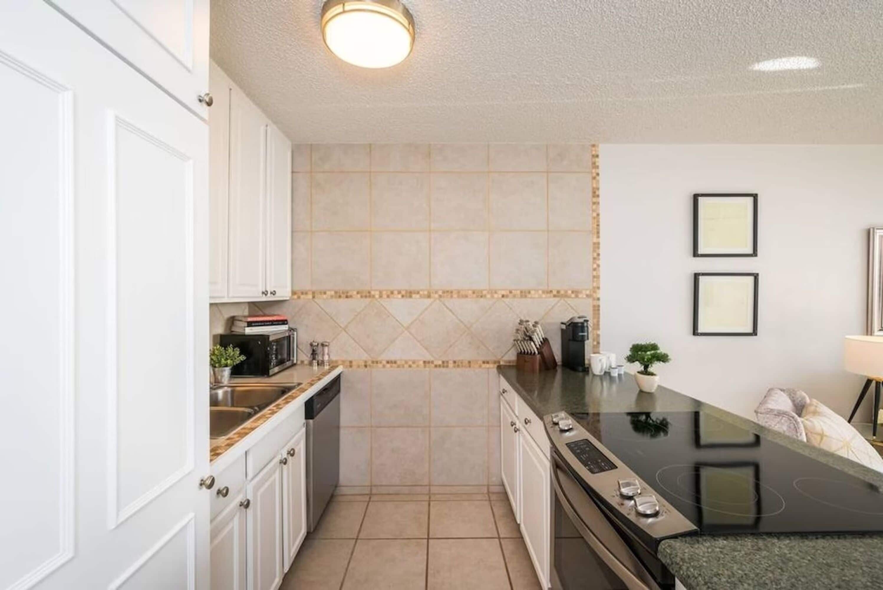 A compact kitchen with white cabinets, a black countertop, and a tiled backsplash.