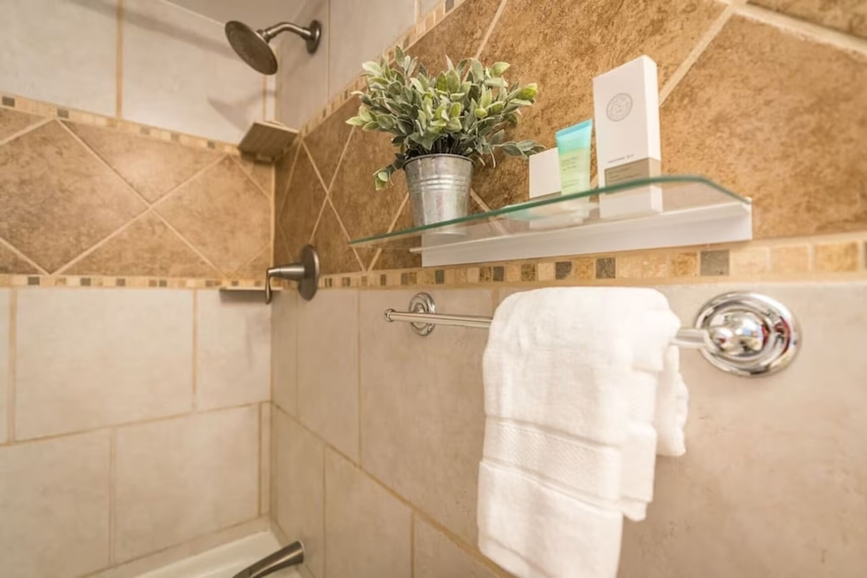 A bathroom with a shower, a glass shelf with toiletries, and a towel rack.