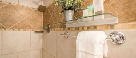Une salle de bain avec une douche, une étagère en verre où sont rangés les articles de toilette et un porte-serviettes.