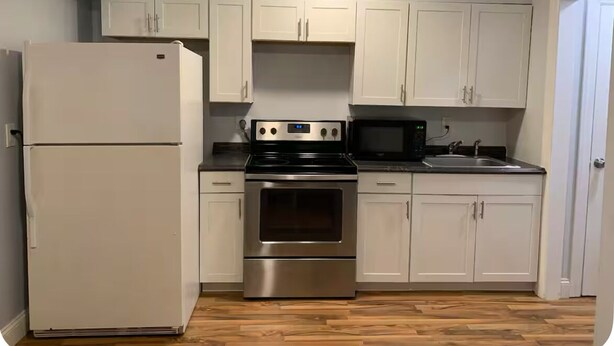 Eine Küche mit weißen Schränken, einem Edelstahlkühlschrank, einer Mikrowelle, einem Backofen und einem Spülbecken.