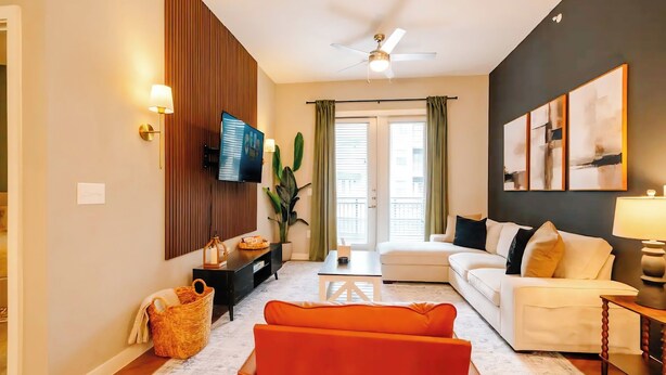 A modern living room with a white sofa, orange armchair, and a flat-screen TV mounted on the wall.