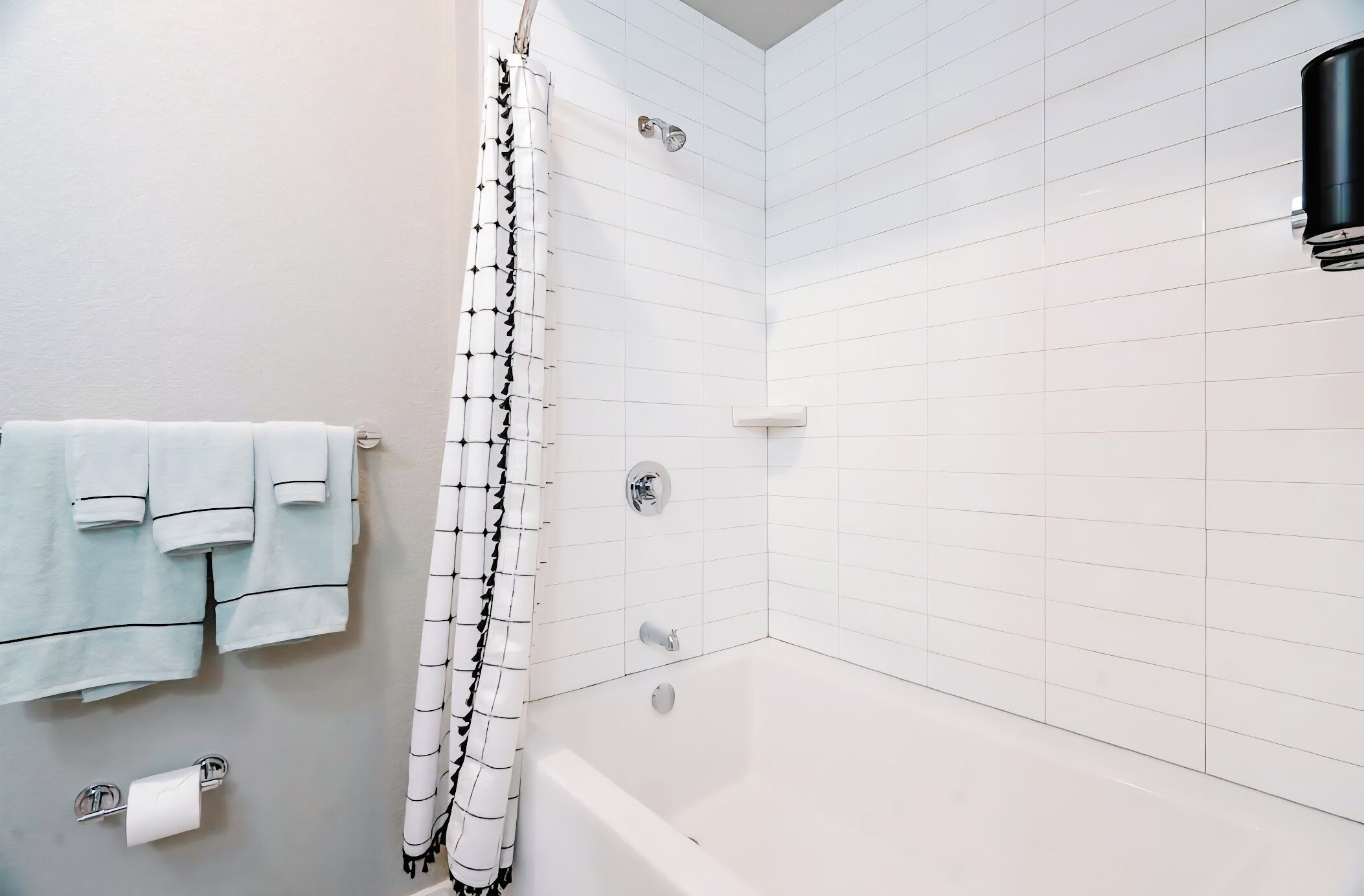 Une salle de bain avec des murs recouverts de carreaux blancs, une baignoire, un rideau de douche et des serviettes accrochées au mur.