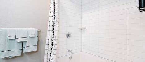 Une salle de bain avec des murs recouverts de carreaux blancs, une baignoire, un rideau de douche et des serviettes accrochées au mur.