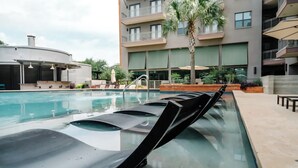 A swimming pool with lounge chairs and a palm tree, surrounded by a modern building with balconies.