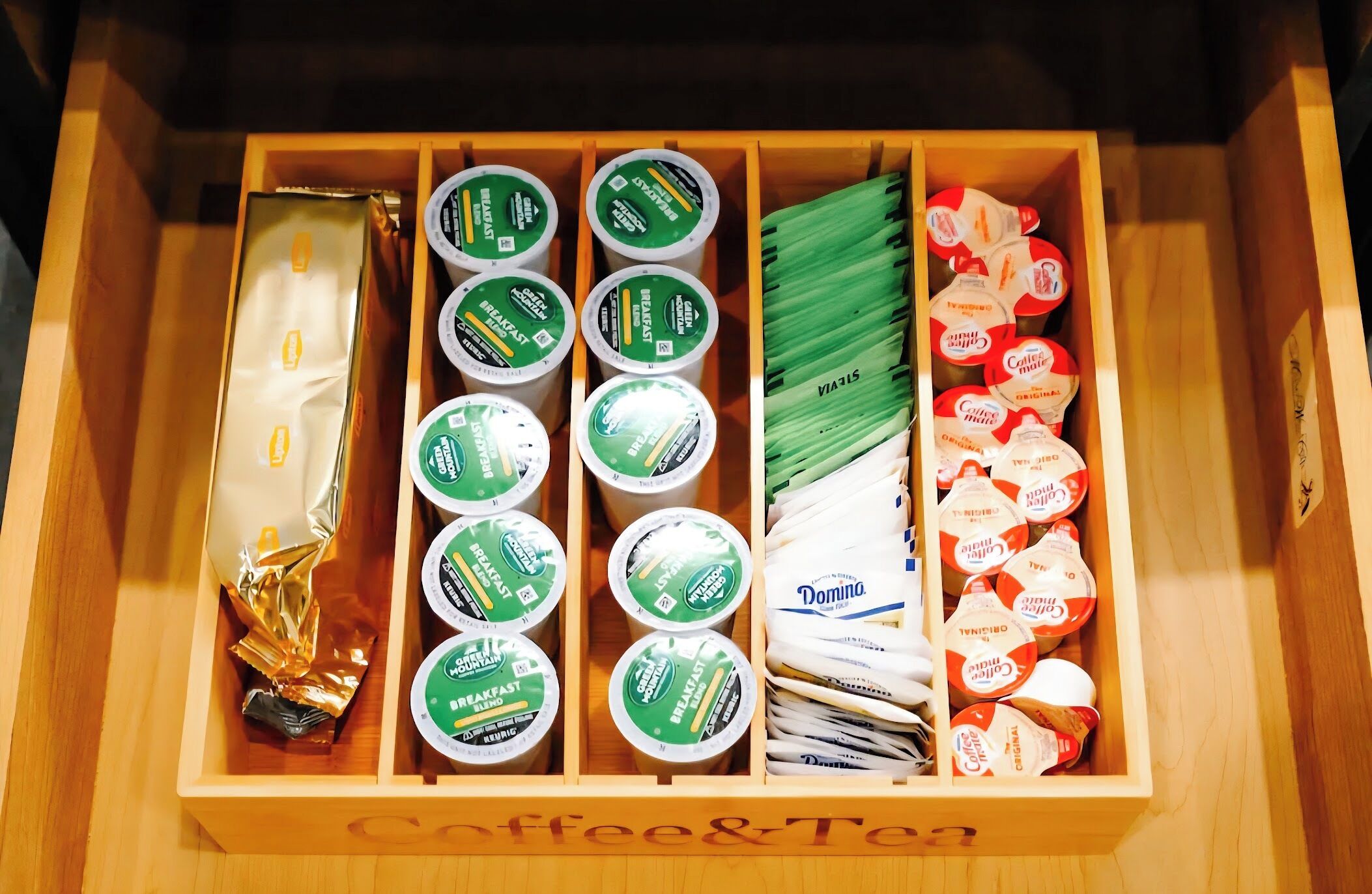 A drawer with compartments containing various coffee and tea products, including branded items and packaged goods.