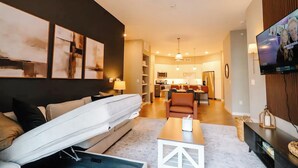 A modern living room with a sofa, a coffee table, and a TV. There is a kitchen in the background.