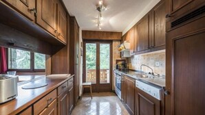 Cucina con pensili in legno, lavello in acciaio inossidabile e zoccolo piastrellato.