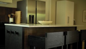 A modern kitchen with a white countertop, dark wooden cabinets, and a bowl of fruit.