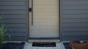 A modern house with a closed front door, a doormat with the word "hello," and a small plant to the left.