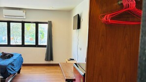 Ein Zimmer mit Bett, Schreibtisch und Fernseher. Es gibt ein Fenster mit Vorhängen, eine Klimaanlage und einen Holzboden.