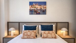 A hotel room with a bed, two nightstands, two lamps, and a wall-mounted picture of a cityscape. - Comfortable 1BR Flat with balcony (Msida)