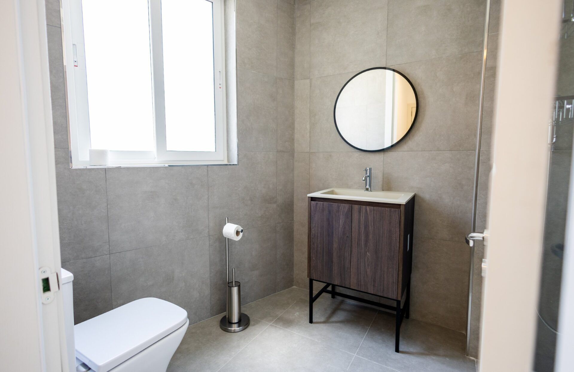 A compact bathroom with a toilet, a sink with a mirror, and a toilet paper holder.