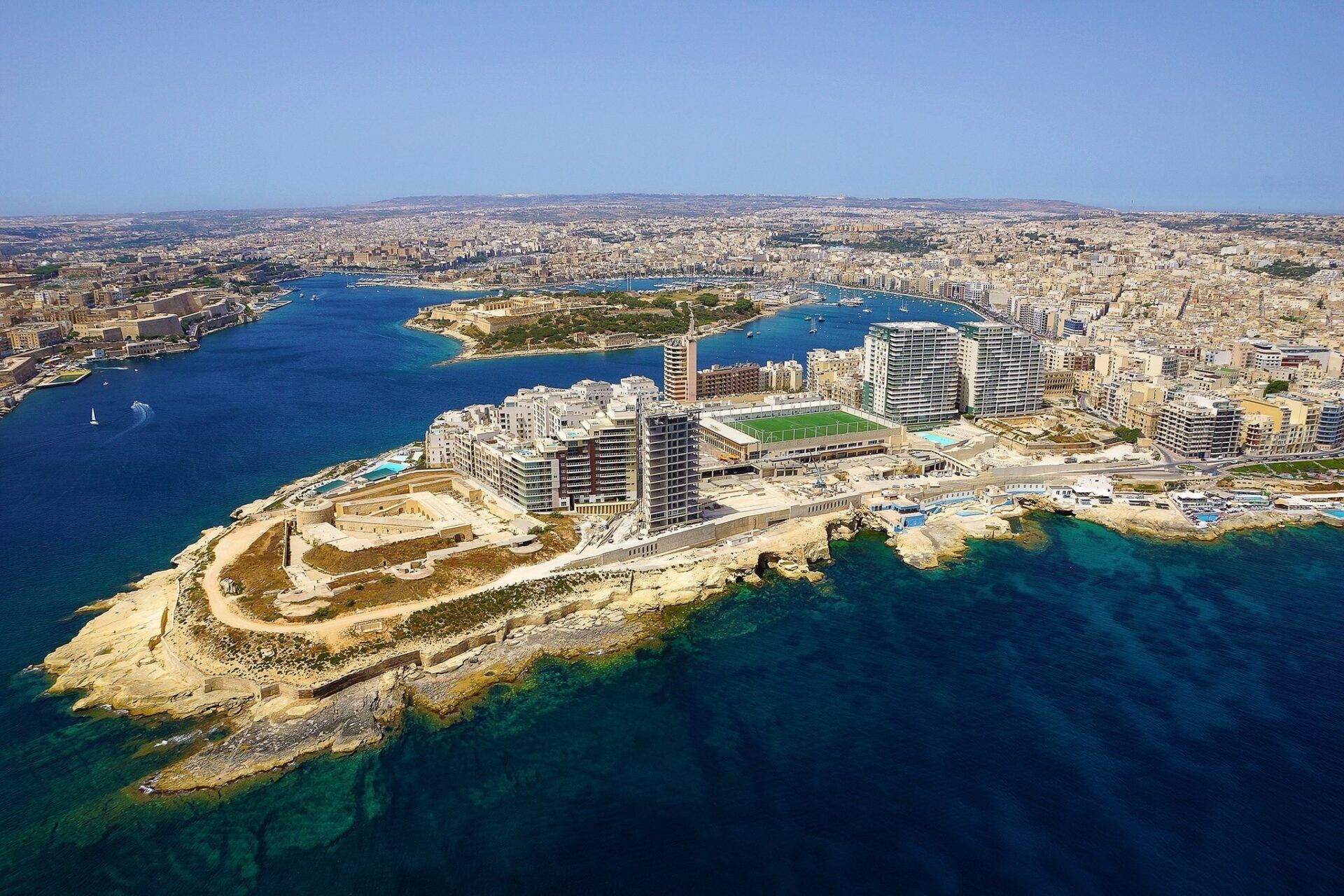 An aerial view of a coastal city with high-rise buildings, a marina, and a rocky coastline.