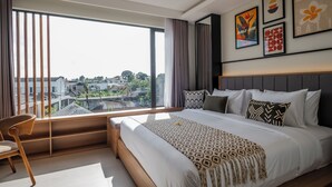 A modern hotel room with a large bed, a view of the city, and artwork on the walls. - TheNomad Canggu – Modern Standard Work Friendly Room in Bali w/ Pool, Gym & Spa (Bali)