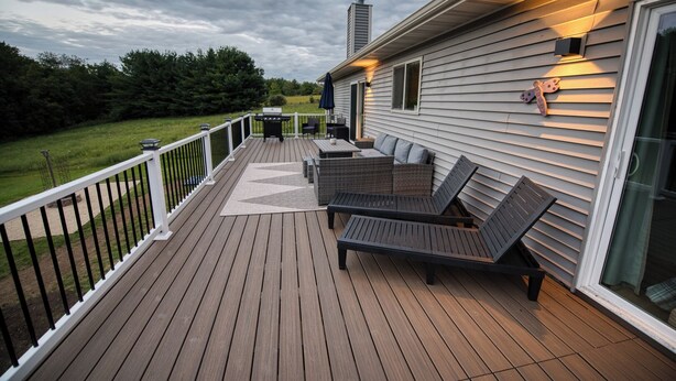 A wooden deck with outdoor furniture, a grill, and a railing.