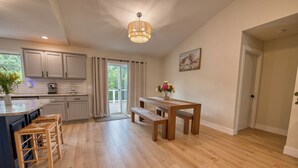 A spacious kitchen with wooden flooring, a central island with bar stools, a dining area with a bench, and a large window with curtains.