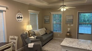 A living room with a gray sofa, a small table with a lamp, and a ceiling fan.