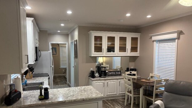 A compact kitchen with white cabinets, a granite countertop, and a coffee station.