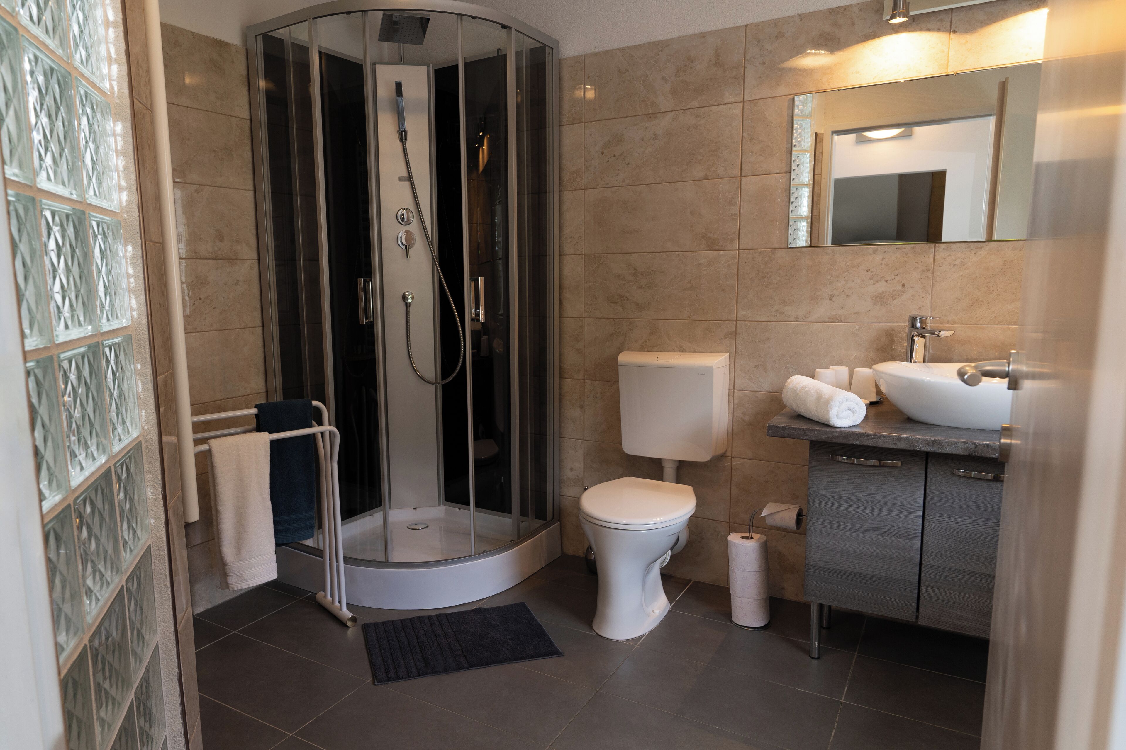 A modern bathroom with a glass-enclosed shower, a toilet, a sink, and a mirror.