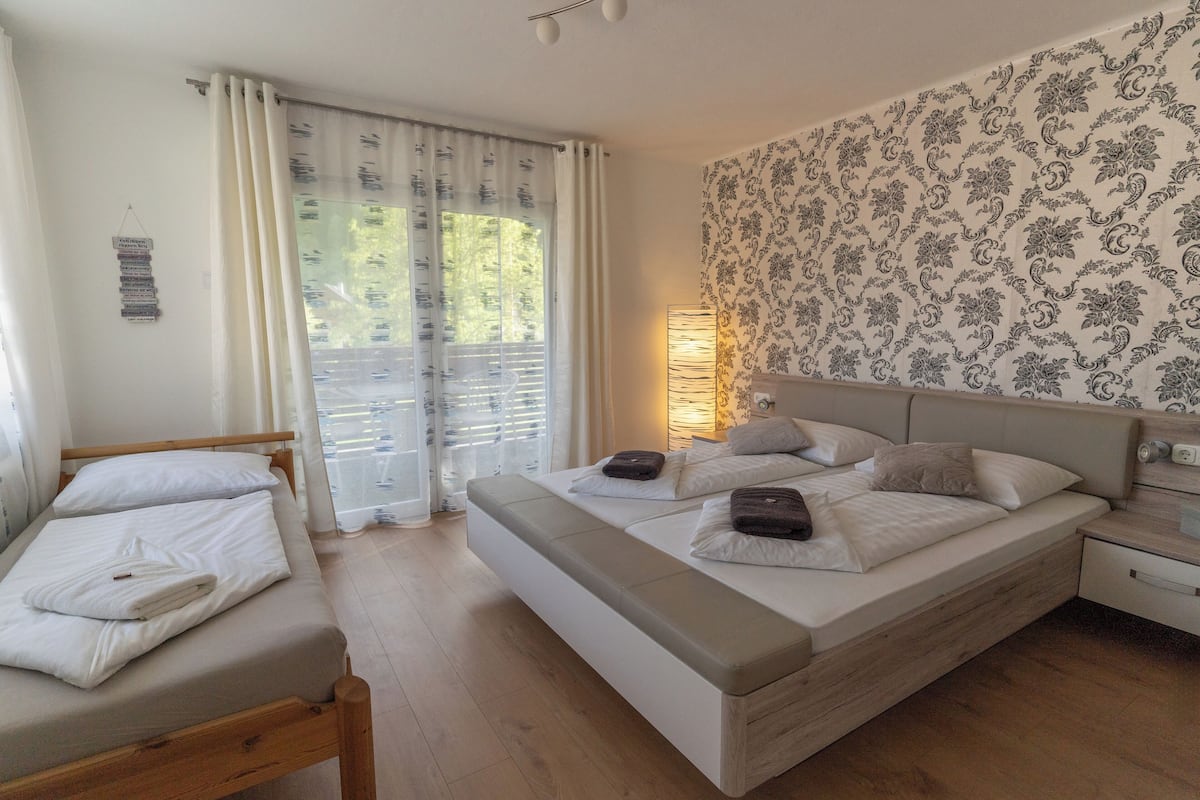 Quarto com cama, mesa de cabeceira e janela com cortinas.