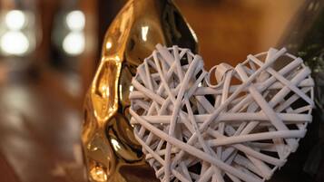 Un vase doré, avec des bâtonnets blancs pour diffuseur d’huiles essentielles et un objet blanc tissé en forme de cœur, posé sur une surface en bois.