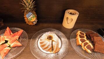 Ein Holztisch mit einer Glasplatte, auf der eine Ananas, Wassermelonenscheiben und eine Kuchenplatte mit Keksen liegen.